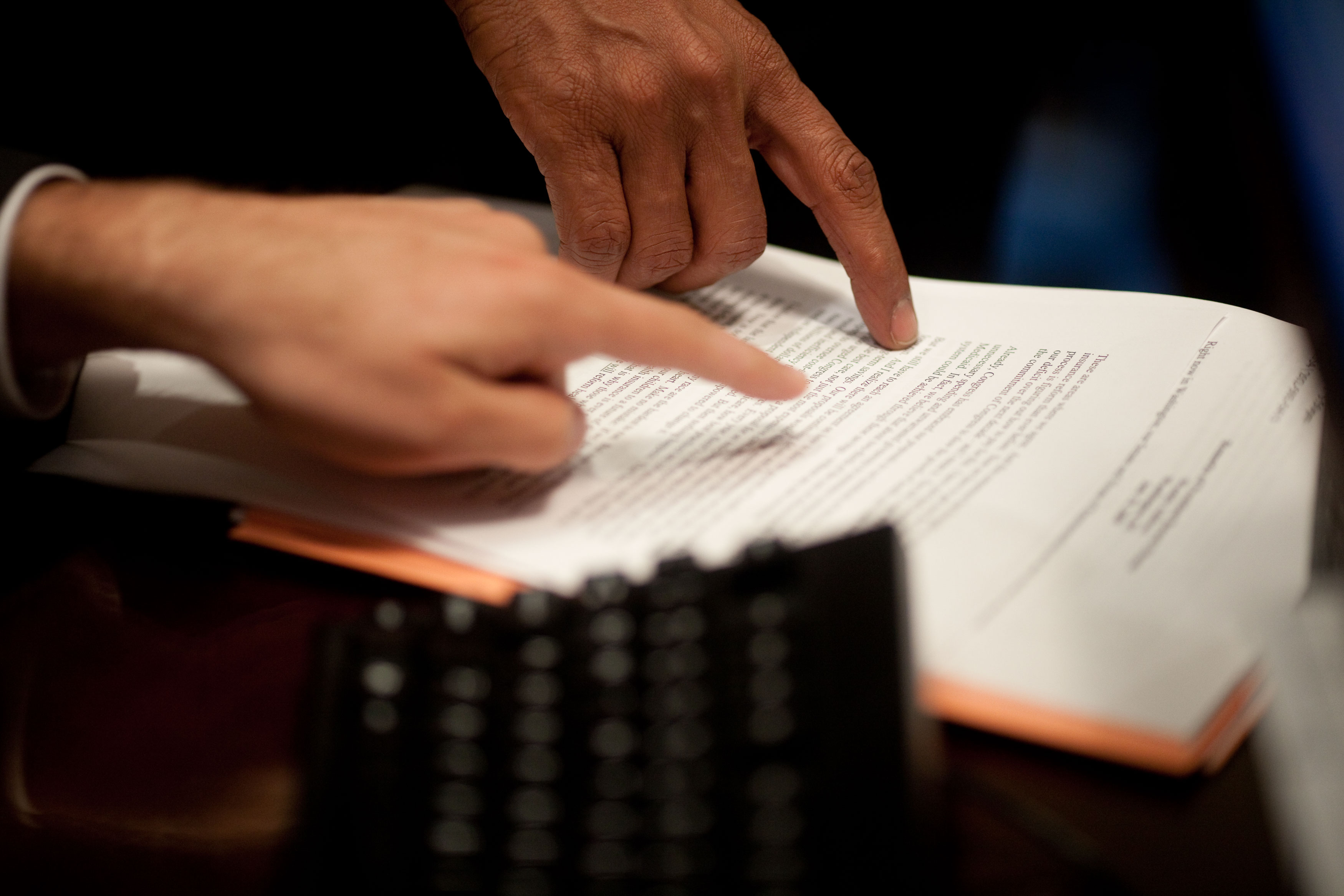 Two hands point at a document on a table.