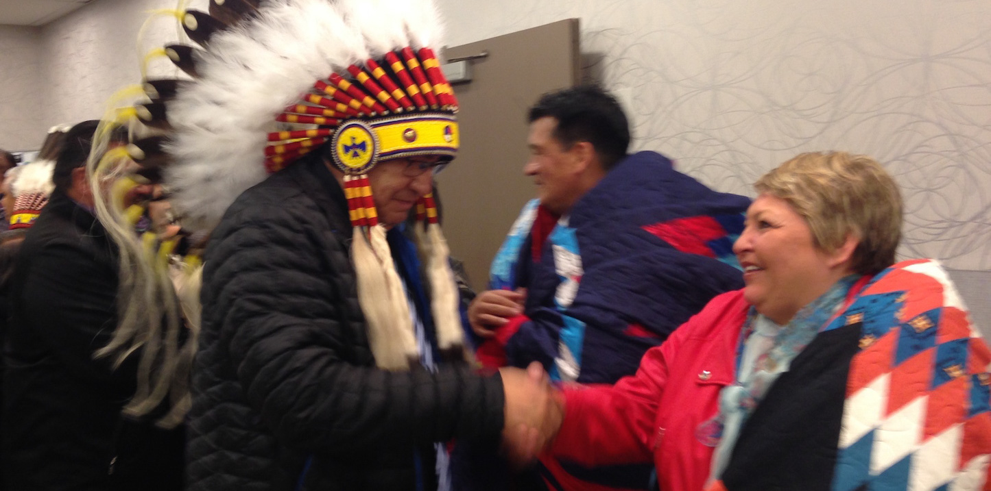 Two First Nations leaders excitedly shake hands.